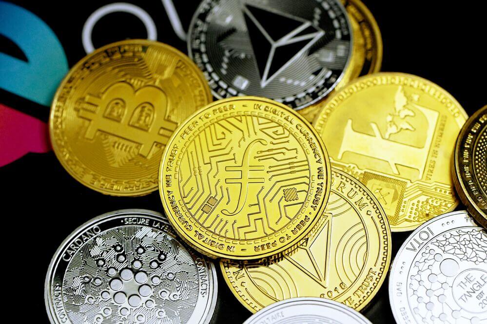 Array of coins bearing cryptocurrency symbols like Cardano, Bitcoin, Ethereum, and more